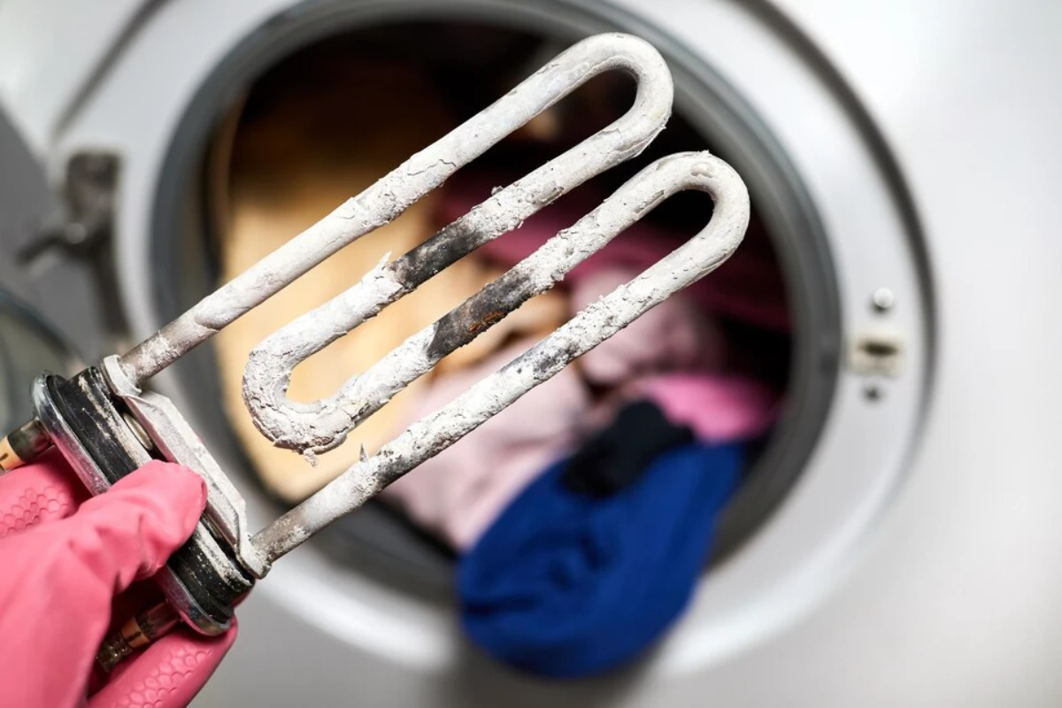 A man holds in his hand a burntout heating element of a washing machine against of a washing machine 