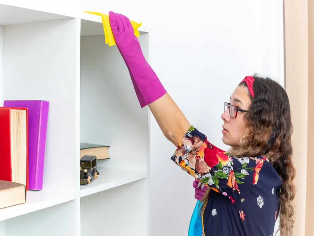 woman rubber gloves wiping white shelves with yellow rag using Daycare Cleaning Checklist
