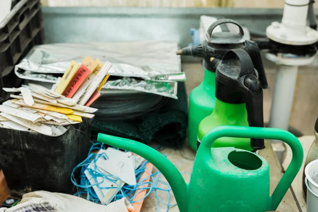 A close-up view of various work supplies, including green spray bottles, a small green watering can, and plant markers.