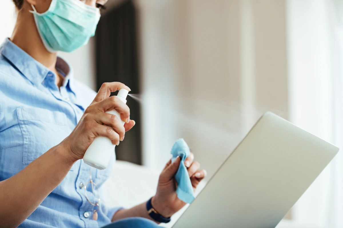 closeup woman using spray bottle while cleaning her laptop virus epidemic