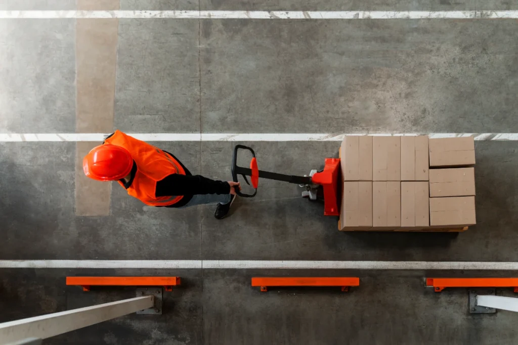 Worker pushing pallet jack with stacked boxes in marked aisle